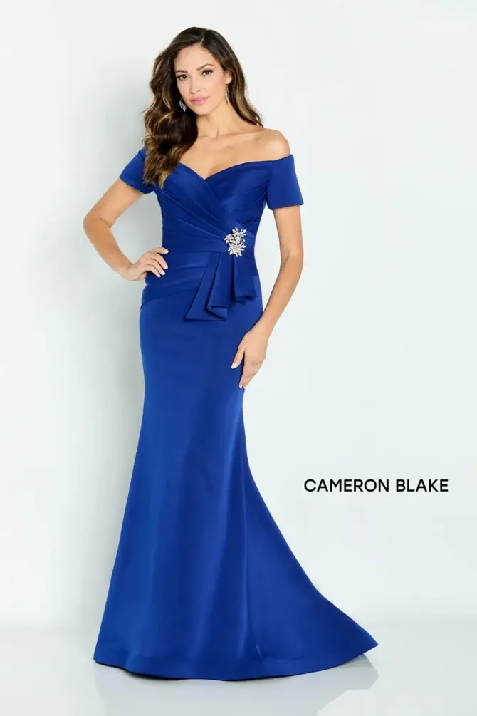 A woman wearing a stylish off-the-shoulder blue evening gown with a fitted silhouette and a decorative bow at the waist.