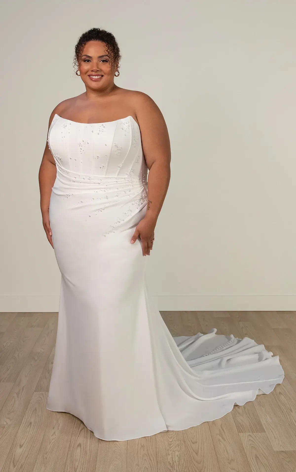 Model is wearing a plus size strapless sheath wedding dress with a long train