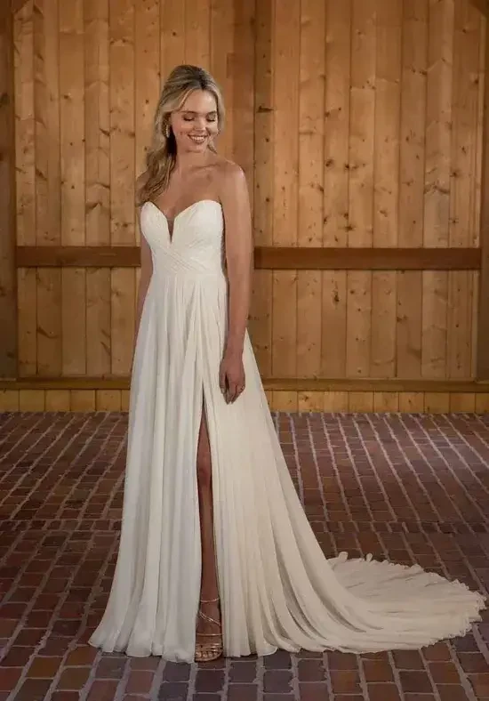 A woman in a white dress with a sweetheart neckline and a thigh-high slit, standing against a wooden wall.