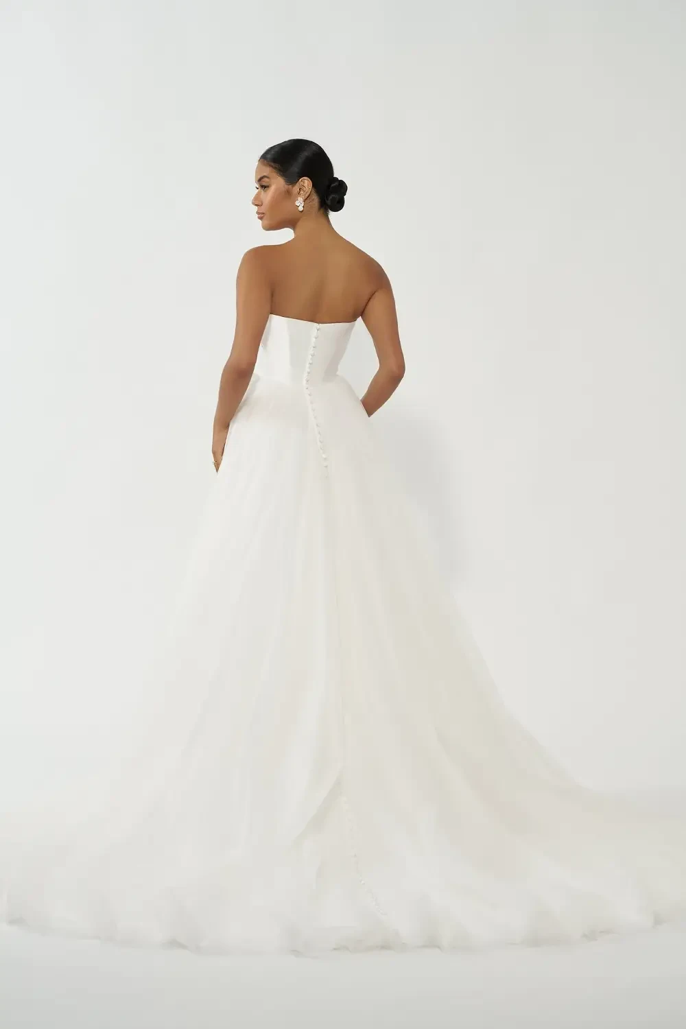 A woman is wearing a strapless white dress with a fitted bodice and a full tulle skirt, posing against a plain background.