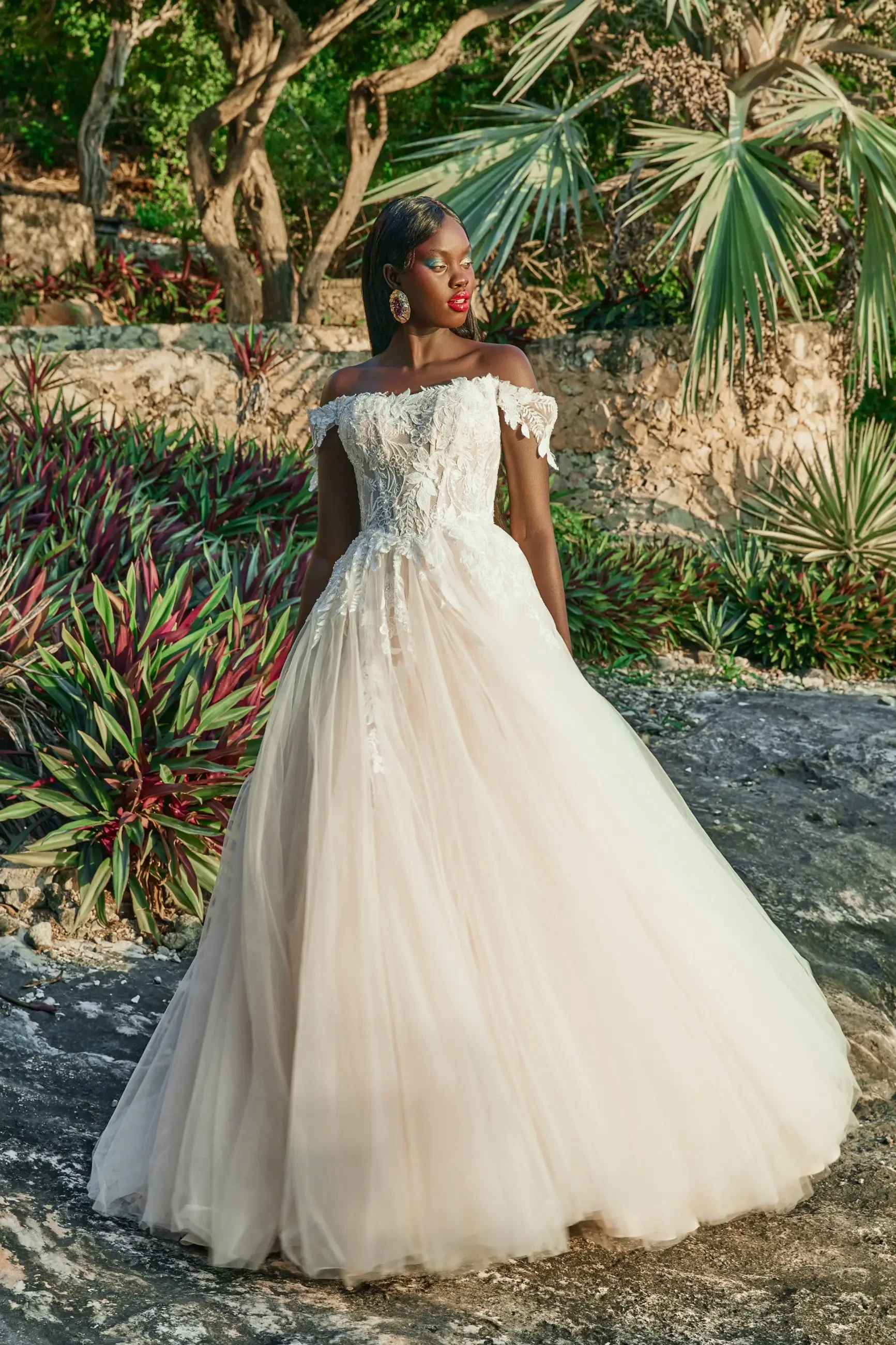 Model is wearing a plus size ball gown off the shoulder wedding dress with a lace bodice