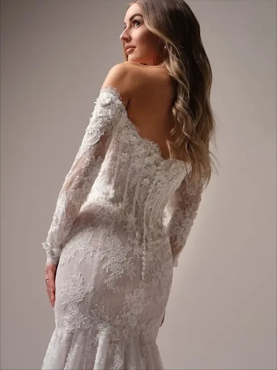 A woman wearing an elegant wedding dress with intricate lace detailing and a long veil, standing gracefully.